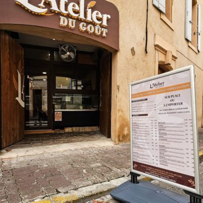 Vue de l'entrée de l'établissement "L'Atelier du Goût" avec un stop trottoir affichant le menu.