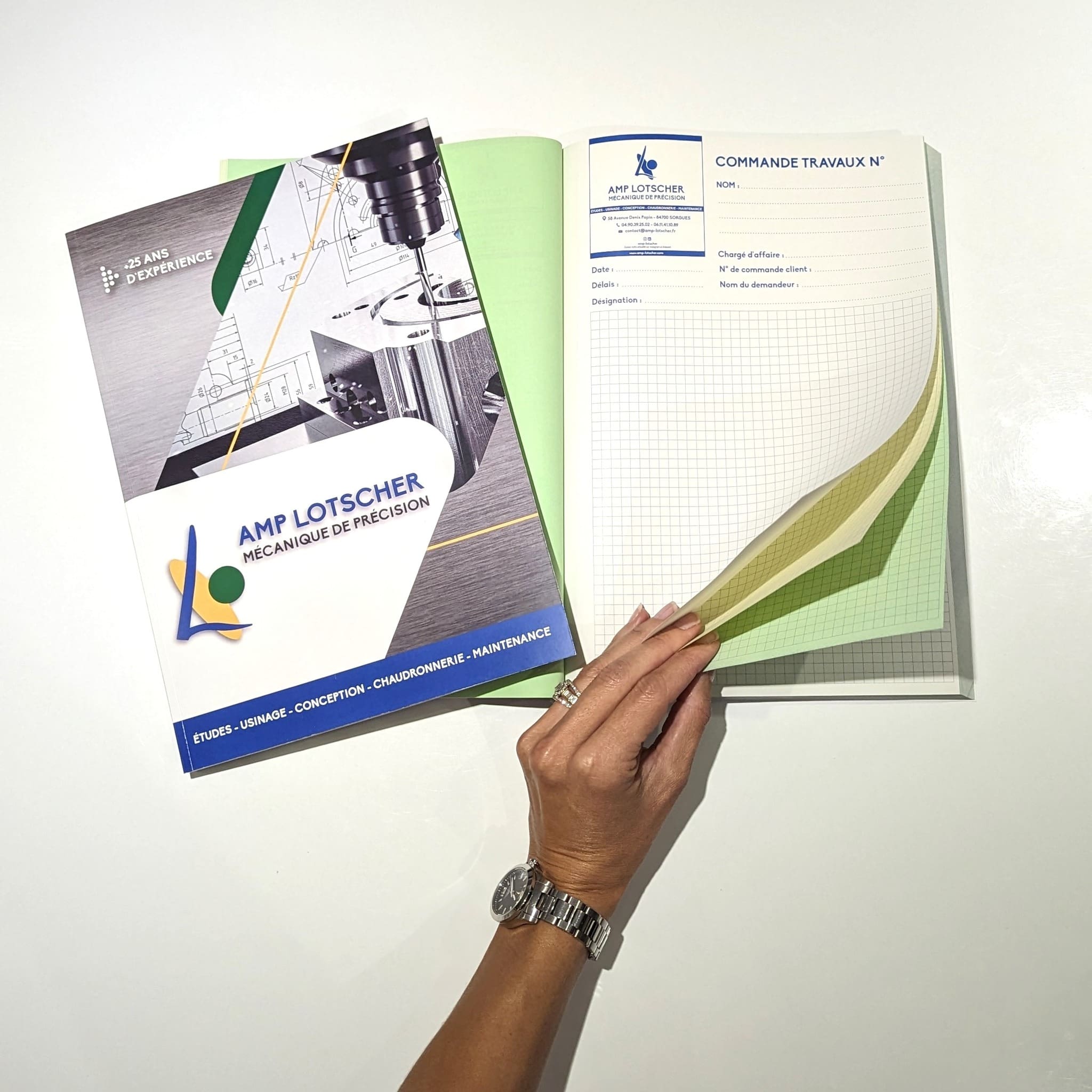 Main feuilletant un carnet de commande AMP Lotscher avec pages en duplicata.