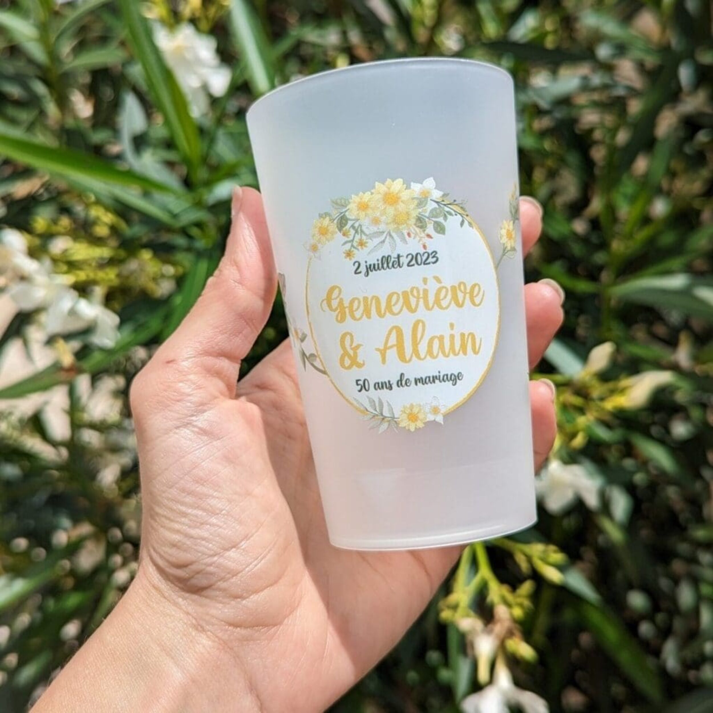 Gobelet personnalisé pour un anniversaire de mariage, tenu en main devant des fleurs