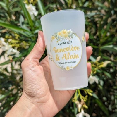 Gobelet personnalisé pour un anniversaire de mariage, tenu en main devant des fleurs