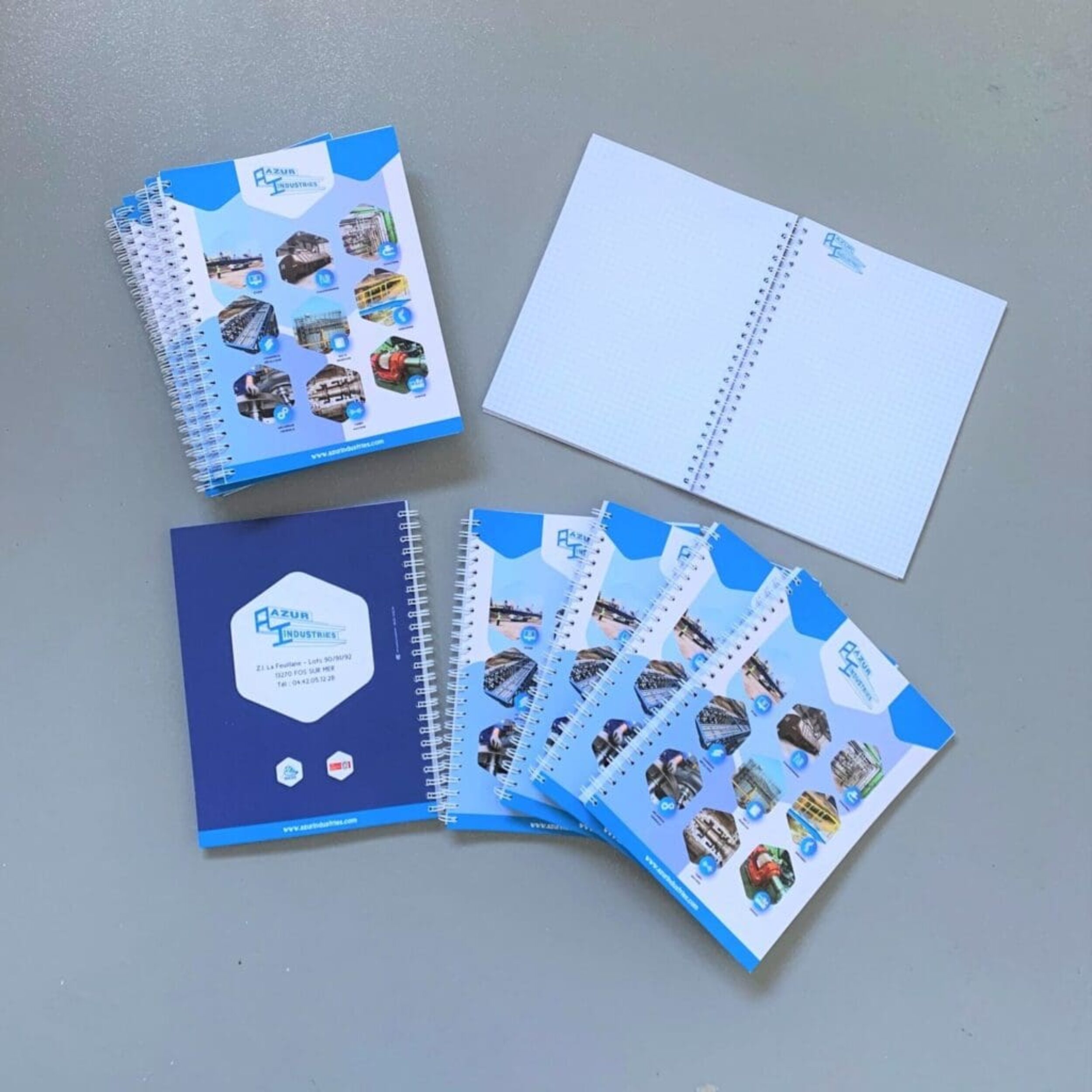 Carnets de notes personnalisés aux couleurs d’Azur Industrie, présentés ouverts et fermés sur fond gris.