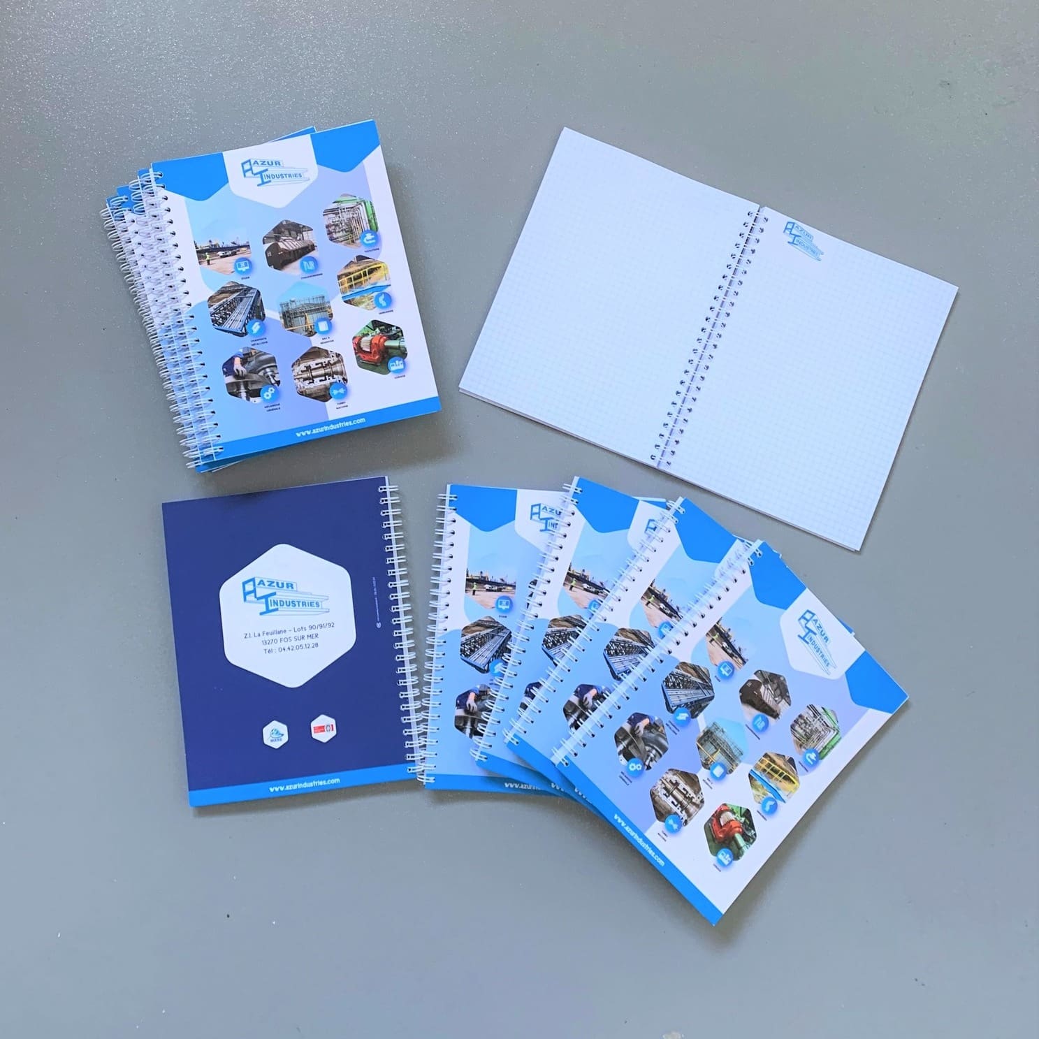 Carnets de notes personnalisés aux couleurs d’Azur Industrie, présentés ouverts et fermés sur fond gris.