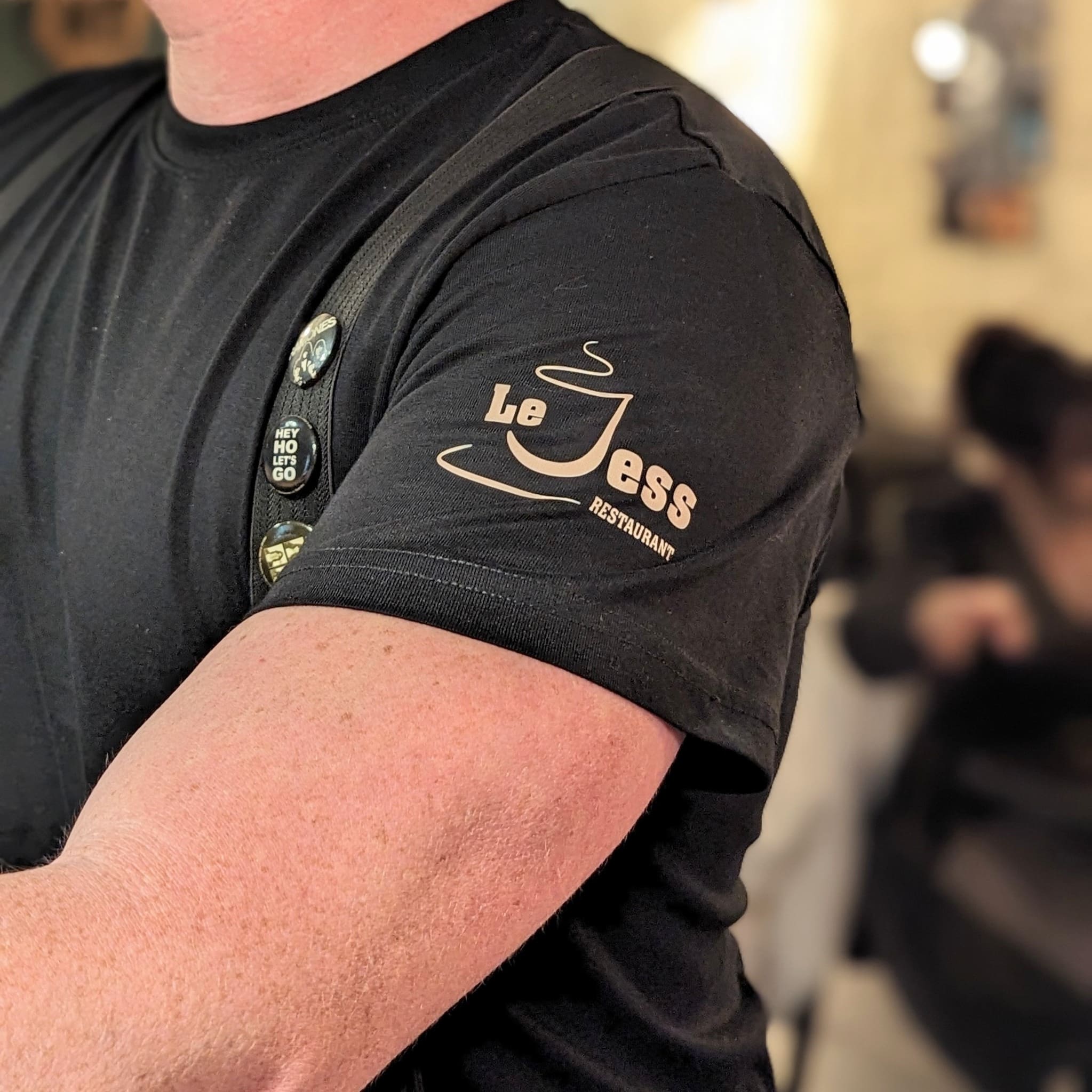 Gros plan sur un t-shirt noir floqué avec le logo du restaurant Le Jess, porté par un membre du personnel.