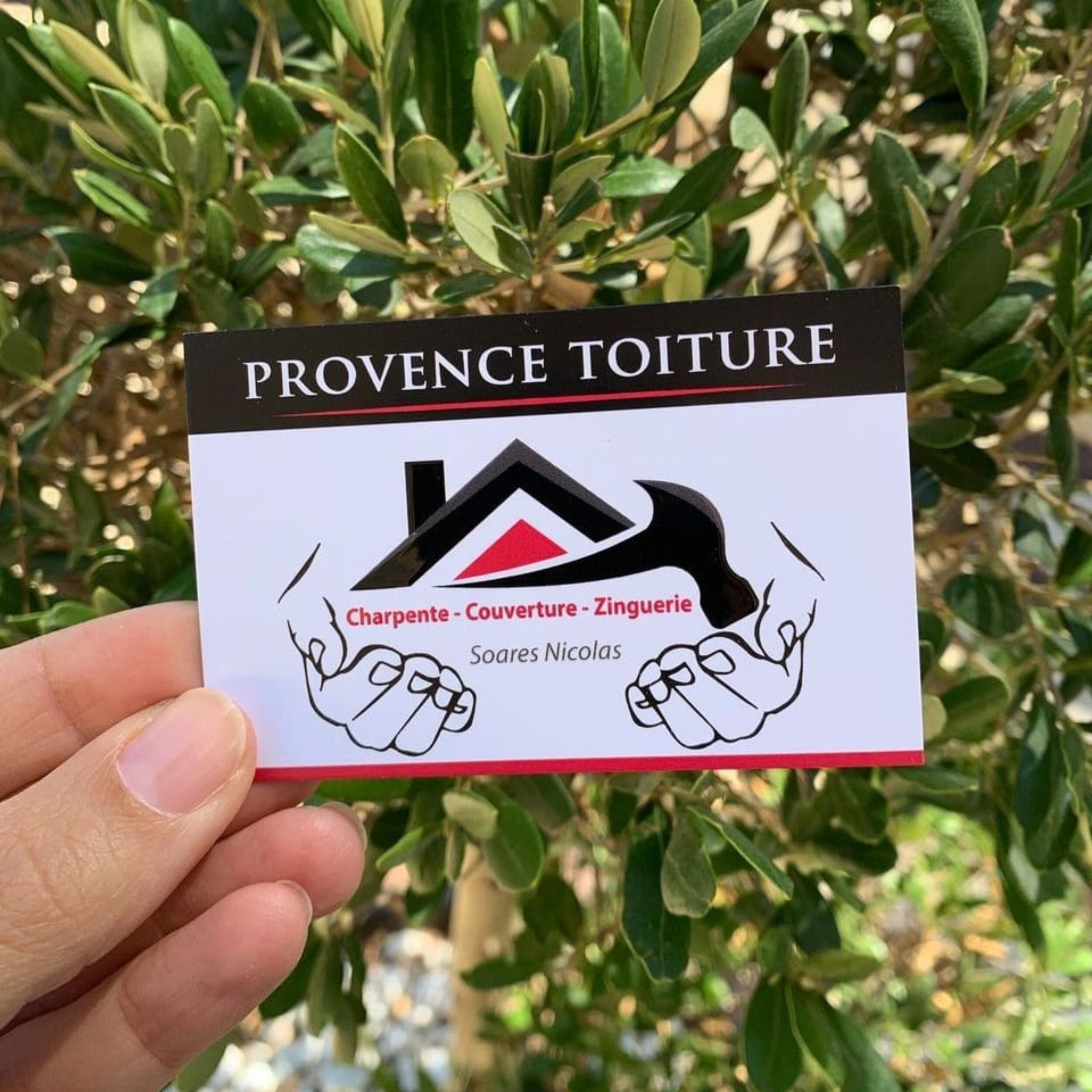 Carte de visite de l’entreprise Provence Toiture, spécialisée en charpente, couverture et zinguerie, tenue en main devant un fond végétal.