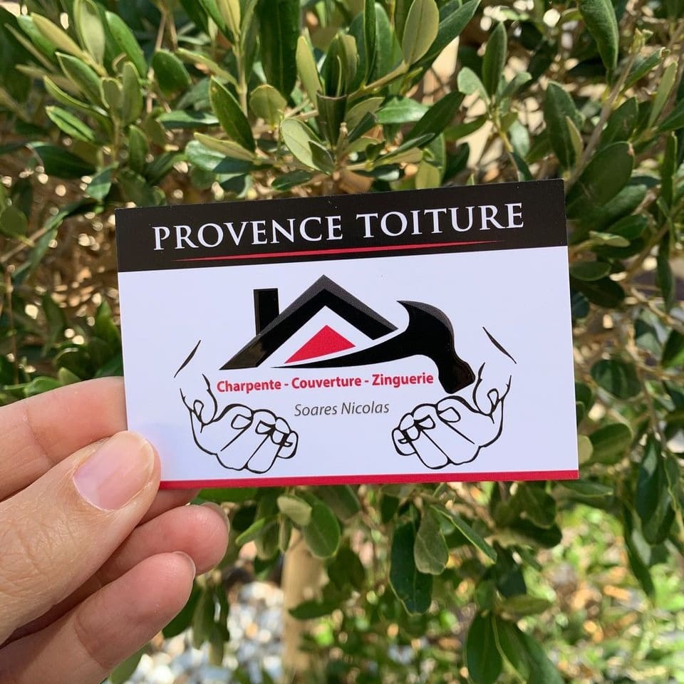 Carte de visite de l’entreprise Provence Toiture, spécialisée en charpente, couverture et zinguerie, tenue en main devant un fond végétal.